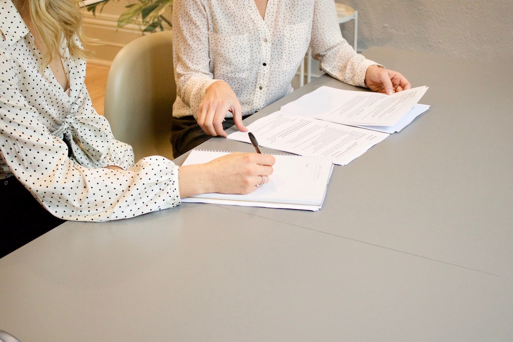 dos mujeres trabajando juntas en una mesa con papeles
